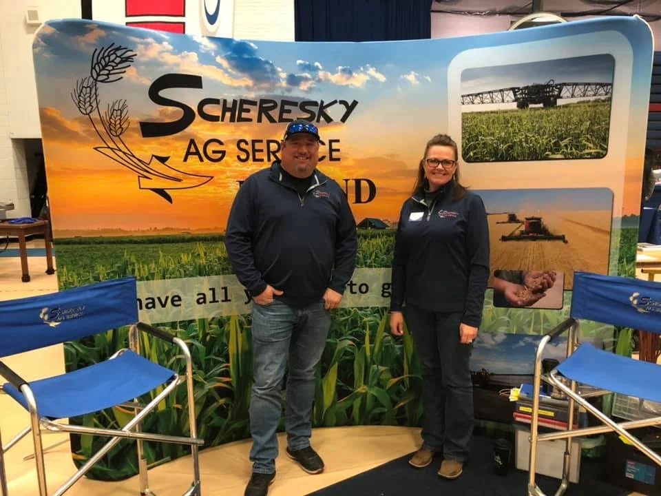 A woman and man standing in a Scheresky Ag booth at a vendor show